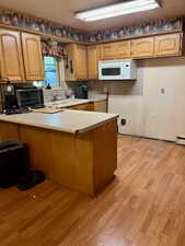 Kitchen with a peninsula, light countertops, light wood finished floors, and white microwave