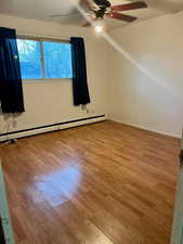 Unfurnished room with wood finished floors, ceiling fan, and baseboard heating