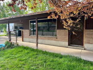 View of exterior entry with brick siding, a carport, and a lawn