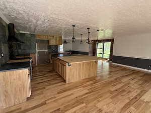 Kitchen featuring light wood-style floors, a large island with sink, electric range, hanging light fixtures, and a textured ceiling