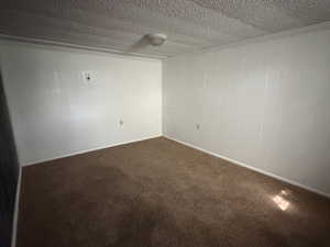 Spare room featuring dark carpet, crown molding, a textured ceiling, and wood walls