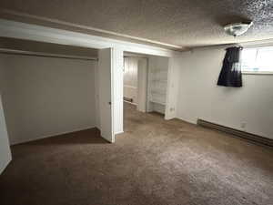 Unfurnished bedroom with a textured ceiling, dark colored carpet, a closet, and a baseboard radiator