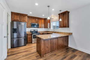 Kitchen with stainless steel appliances, light stone counters, a peninsula, pendant lighting, and dark wood-style floors