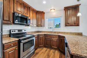 Kitchen with stainless steel appliances, pendant lighting, light wood-style floors, and light stone counters