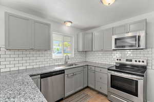 Kitchen with gray cabinets, stainless steel appliances, light stone counters, and light wood-type flooring