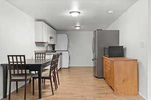 Kitchen featuring light countertops, light wood-type flooring, stacked washer / dryer, white cabinetry, and freestanding refrigerator