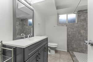 Full bath featuring tiled shower, vanity, and light tile patterned floors