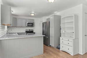 Kitchen with gray cabinets, stainless steel appliances, light wood-style floors, and a peninsula