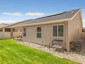 Rear view of house featuring a fenced backyard, a shingled roof, roof mounted solar panels, and a patio area