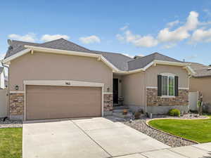 Single story home with stone siding, stucco siding, an attached garage, concrete driveway, and a front lawn