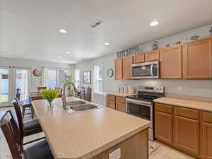 Kitchen featuring stainless steel appliances, a center island with sink, light countertops, recessed lighting, and light tile patterned floors
