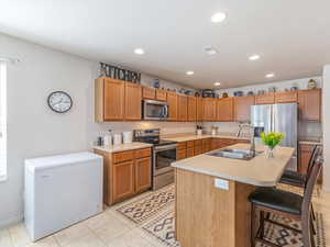 Kitchen featuring stainless steel appliances, light countertops, an island with sink, a breakfast bar, and light tile patterned floors