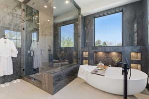 Bathroom featuring a freestanding bath, a marble finish shower, and tile walls