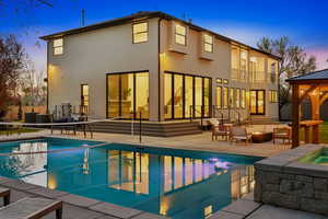 Back of house at dusk featuring a patio, a hot tub, an outdoor pool, gazebo, fire pit