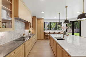 Kitchen featuring dark stone counters, light wood finished floors, black electric stovetop, and light wood finish cabinets
