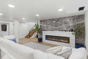 Living room with a glass covered fireplace, light wood-style floors, recessed lighting, and an accent wall