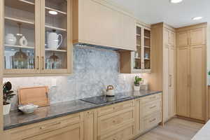 Kitchen featuring glass insert cabinets, dark stone counters, light wood finish cabinets, backsplash, and recessed lighting