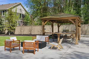 Fenced backyard with a fire pit, a patio area, an outdoor kitchen with living area, and a gazebo