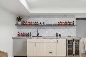 Indoor wet bar with light wood finish cabinetry, open shelves, dishwasher, and beverage cooler
