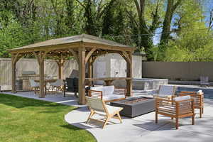 Fenced backyard with a patio, a gazebo, a fire pit, and an outdoor kitchen and area to lounge