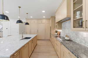 Kitchen with light stone countertops, a spacious island, light wood-style floors, light wood finish cabinetry, and decorative backsplash