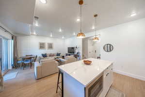 Open-concept living space featuring a kitchen island with stone-finish countertop, pendant lighting, wood-finish flooring, recessed lighting, and sliding glass door access to an exterior area