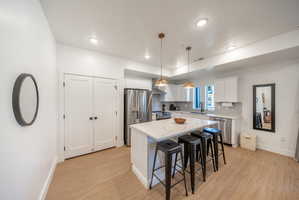 Modern kitchen featuring an island with a light-colored countertop, stainless steel appliances, white cabinetry, recessed lighting, and wood-finish flooring