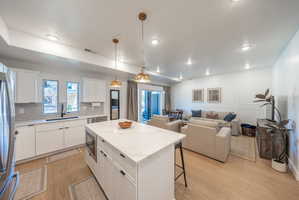 Open-concept living area featuring a kitchen island with stone-finish countertop, wood-finish flooring, recessed lighting, and wall paneling