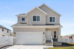 View of front of house featuring stone, stucco siding,  a shingled roof, a gate, and concrete driveway.