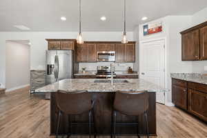 Kitchen featuring granite counters, wood cabinetry, stainless steel appliances, and a kitchen island with sink