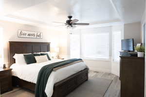 Bedroom featuring a tray ceiling, a textured ceiling, wood finished floors, multiple windows, and ceiling fan