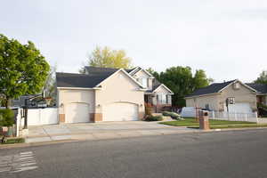 View of front of house with an attached garage, brick siding, concrete driveway, stucco siding, and a gate