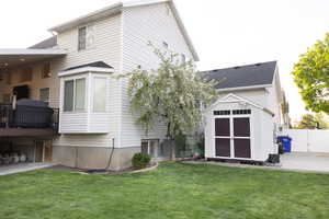 Back of house with a shed, a patio area, and roof with shingles