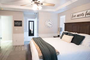 Bedroom with light wood-style floors, crown molding, ceiling fan, and a raised ceiling