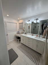 Bathroom with double vanity, a walk in closet, a textured ceiling, a stall shower, and light tile patterned floors