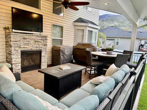 View of patio with a deck with mountain view, an outdoor stone fireplace, ceiling fan, and an outdoor lounge area with bar