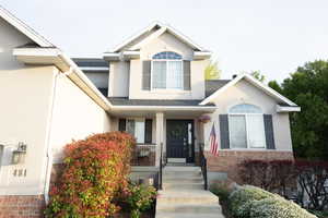 View of front of property featuring covered porch, stucco siding, a shingled roof, and brick siding