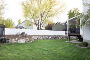 Fenced backyard featuring a wooden deck, a trampoline, and a patio