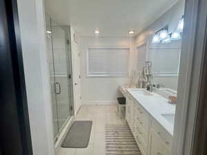 Bathroom with double vanity, a stall shower, a textured ceiling, and recessed lighting