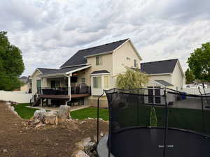 Back of house featuring a trampoline, a fenced backyard, roof with shingles, a deck, and a storage unit
