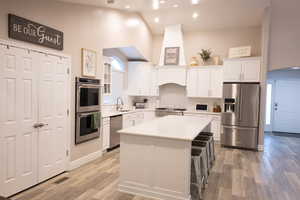 Kitchen featuring white cabinetry, stainless steel appliances, vaulted ceiling, a kitchen island, and light wood finished floors