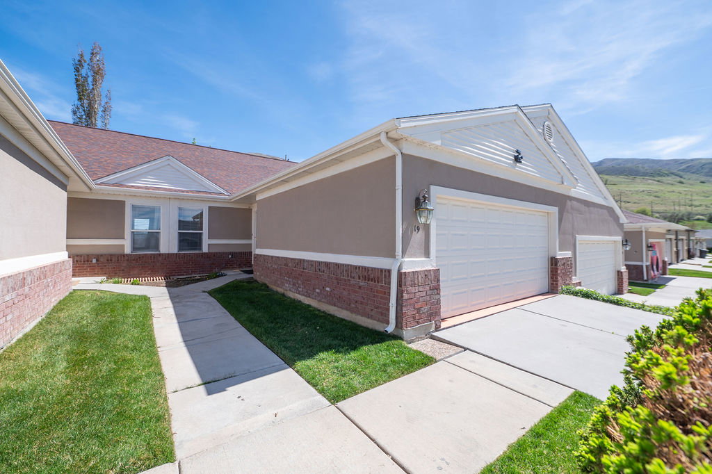 View of property exterior with an attached garage, brick siding, concrete driveway, and a yard