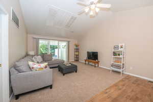 Living area with lofted ceiling, ceiling fan, and new carpet, showing sliding glass door that leads to the private back yard.