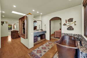 Hallway with light wood-type flooring, recessed lighting, arched walkways, and a skylight