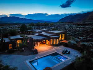 Back of house at dusk with an in-ground hot tub, a mountain view, and a patio