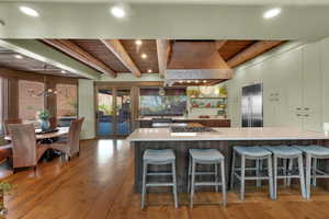Kitchen with a kitchen breakfast bar, stainless steel appliances, a wooden ceiling with exposed beams, hanging lights, and light wood-style flooring