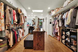 Walk in closet with arched walkways, light wood finished floors, and a skylight