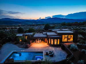 Back of house at dusk featuring a mountain view, an in-ground hot tub, and a patio area