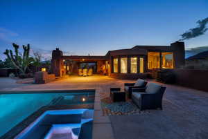 Back of property at dusk featuring a patio area, stucco siding, a pool with connected hot tub, and an outdoor hangout area