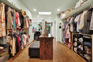 Walk in closet with arched walkways, light wood finished floors, and a skylight